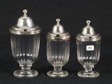 three clear glass jars with silver lids on a black background