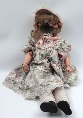 an old fashioned doll sitting on a white surface wearing a dress and hat