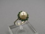 un gros plan d'une bague ornée d'une perle et de pierres vertes
