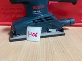 une ponceuse orbitale Bosch posée sur une table, à côté d'une boîte rouge