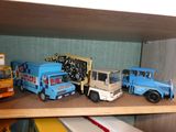 Plusieurs camions miniatures sont alignés sur une étagère dans une pièce