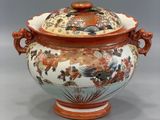 an orange and white vase with a lid with flowers on it