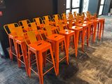 rows of orange metal stools in a room with a black wall