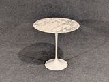 une table en marbre blanc avec un piètement blanc, posée sur un tapis gris