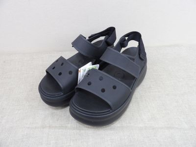 La sandale est noire et comporte deux lanières de chaque côté.