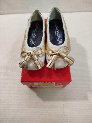 une paire de chaussures blanches et dorées ornées de nœuds, posée sur une boîte rouge