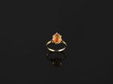 a gold ring with an orange stone on a black surface