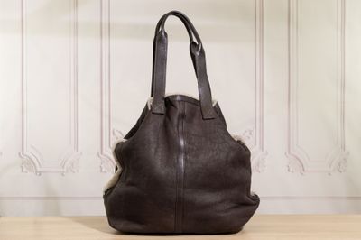 un sac à main en cuir marron posé sur une table en bois devant un mur blanc