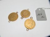 trois pièces d'or sont posées sur une surface blanche, accompagnées d'une étiquette de prix