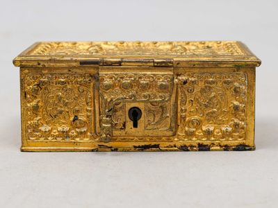 une vieille boîte dorée ornée de sculptures, posée sur une surface blanche