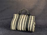un sac à main rayé beige et noir posé contre un mur gris