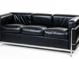 black leather sofa with chrome legs and arm rests against a white background