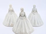 three white ceramic figurines of brides on a white background