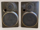 two black speakers with gold trims sit side by side on a white surface
