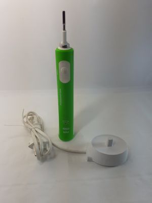 une brosse à dents électrique verte et un chargeur posés sur une table blanche