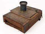 an old wooden box with a metal cup on top