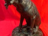 statue en bronze représentant un chien assis sur un socle, sur fond rouge