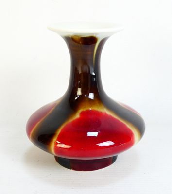 un vase rouge et noir posé sur une surface blanche
