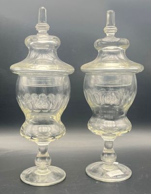 two clear glass vases with lids on a black surface