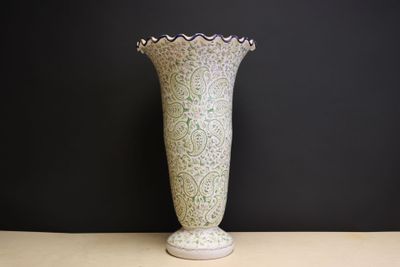 a white vase sitting on a table with a black wall in the background