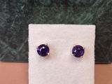 une paire de boucles d'oreilles en pierre violette posées sur un tissu blanc