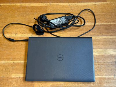 un ordinateur portable Dell avec son cordon d'alimentation et son chargeur, posé sur un plancher en bois