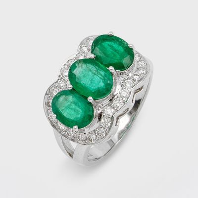 une bague à trois pierres, composée d'une émeraude et de diamants, sur fond blanc