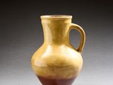 un vase jaune et rouge posé sur une surface grise, sur fond noir