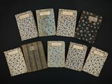 six petits cahiers sont alignés sur une surface noire