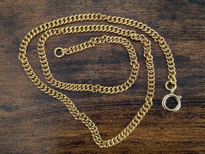 a close up of a gold chain with a ring on a wooden table