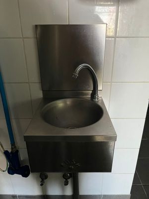 un lavabo en acier inoxydable dans des toilettes publiques, équipé d'un tuyau bleu