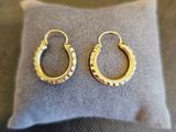 des boucles d'oreilles créoles plaquées or posées sur un coussin gris