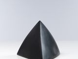 un objet noir en forme de pyramide posé sur une surface blanche