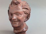 statue représentant la tête d'une femme aux cheveux bouclés, posée sur une surface grise