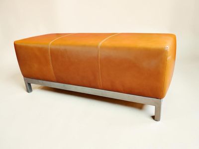 une banquette en cuir orange avec des pieds en métal, sur fond blanc