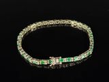 a close up of a bracelet with emerald stones on a black surface