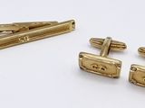 two pairs of gold cufflinks and a tie bar on a white surface