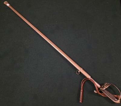 une vieille canne en bois avec un pommeau en métal sur un fond noir