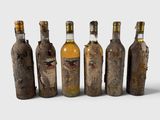 six bouteilles d'alcool sont alignées sur une surface blanche