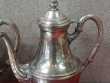 une théière en argent et une assiette en argent posées sur une nappe rouge