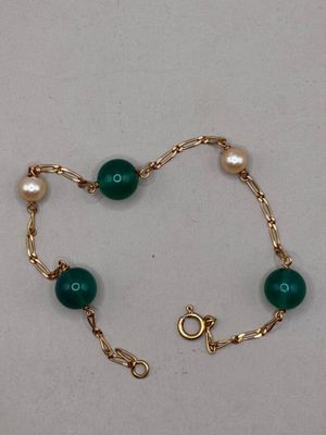 un gros plan sur un bracelet en or orné de perles vertes et de perles de culture