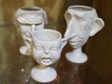 trois vases blancs ornés de visages, posés sur une table en verre