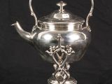 silver plated teapot on stand with handle on black background