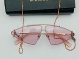 a pair of pink sunglasses with gold chain on a white surface
