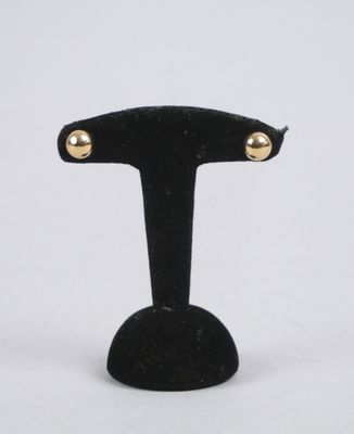 pair of gold tone studded earrings on a black velvet stand
