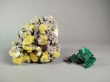 yellow and green crystals on a white surface next to a green piece of rock