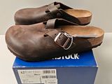 pair of brown clogs sitting on top of a box on a white surface