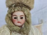 a doll that is wearing a fur hat and a sweater