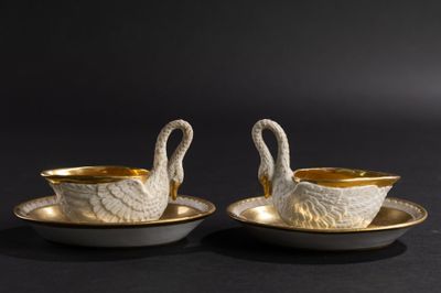 deux assiettes en forme de cygne, blanches et dorées, posées sur un fond noir