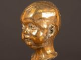une statue en or représentant la tête d'un homme, posée sur un socle en marbre noir